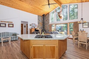 A spacious living area with a large wooden ceiling, a stone wall, and a view of the forest through large windows.