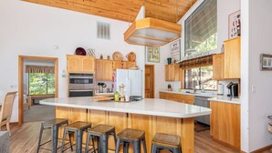 Una cocina moderna con armarios de madera, una isla central con taburetes, electrodomésticos de acero inoxidable y una lámpara colgante.