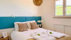 A neatly made bed with patterned pillows, a bedside table with a framed quote, and a window with a view of greenery. - Unique Romantic Beach House by the Atlantic Ocean (Colares)