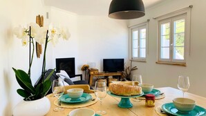 A dining area with a wooden table set for four, featuring teal plates and bowls, a loaf of bread, and a bottle of olive oil. - Unique Romantic Beach House by the Atlantic Ocean (Colares)