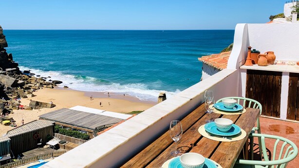 A wooden table with blue plates and wine glasses, overlooking a beach with rocky cliffs and the ocean. - Unique Romantic Beach House by the Atlantic Ocean (Colares)