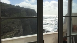 A room with a large window overlooking a rocky coastline and the sea. - Unique Romantic Beach House by the Atlantic Ocean (Colares)