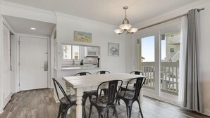 Un coin repas avec une table et des chaises en bois, une cuisine à l’arrière-plan et un balcon avec des rideaux.