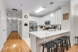 A modern kitchen with white cabinetry, stainless steel appliances, and a central island with bar stools. - River & Marsh Views - Pool, Walk to Downtown Folly, Pet Friendly w/fee - Marshwinds! (Folly Beach)