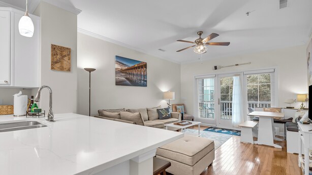 A modern kitchen with a large island, a dining area with a table and chairs, a sofa, and a ceiling fan. - River & Marsh Views - Pool, Walk to Downtown Folly, Pet Friendly w/fee - Marshwinds! (Folly Beach)