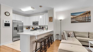 A modern kitchen with white cabinets, a stainless steel refrigerator, and a central island with stools. - River & Marsh Views - Pool, Walk to Downtown Folly, Pet Friendly w/fee - Marshwinds! (Folly Beach)