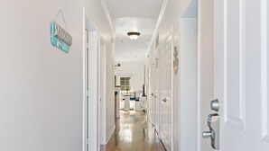 A hallway with white walls and wooden flooring leading to a kitchen area. - River & Marsh Views - Pool, Walk to Downtown Folly, Pet Friendly w/fee - Marshwinds! (Folly Beach)