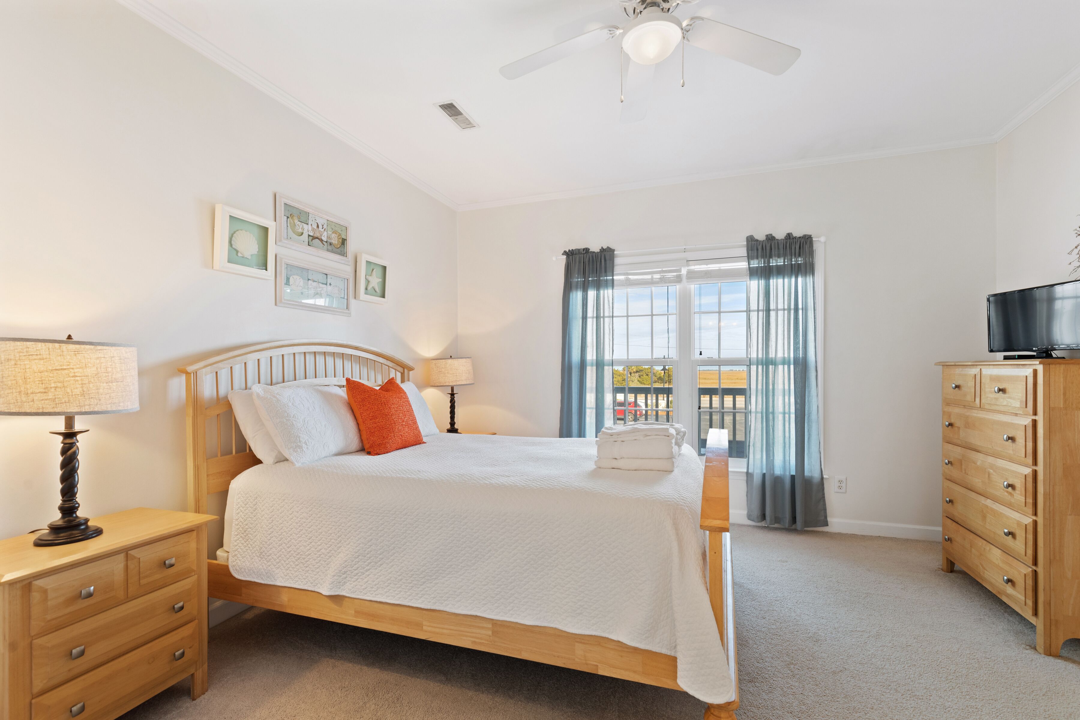 A bedroom with a bed, nightstands, a dresser, a ceiling fan, and a window with curtains.