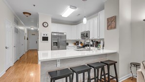A modern kitchen with white cabinetry, a stainless steel refrigerator, a microwave, and a large island with bar stools. - River & Marsh Views - Pool, Walk to Downtown Folly, Pet Friendly w/fee - Marshwinds! (Folly Beach)