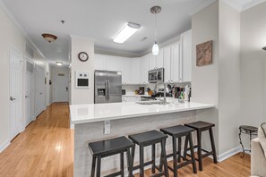 A modern kitchen with white cabinetry, a stainless steel refrigerator, a microwave, and a large island with bar stools. - River & Marsh Views - Pool, Walk to Downtown Folly, Pet Friendly w/fee - Marshwinds! (Folly Beach)