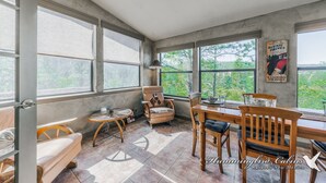 Una habitación amplia con ventanas grandes, una mesa de comedor de madera y un rincón de descanso acogedor.