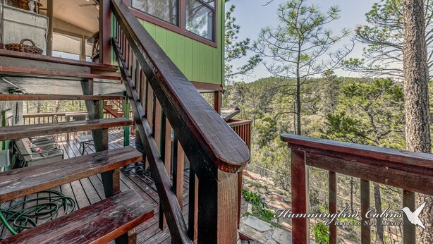 Una cabaña con una escalera de madera que lleva a una terraza, rodeada de árboles.