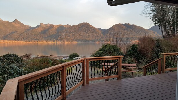 Une terrasse en bois avec une rambarde donnant sur un lac et des montagnes.