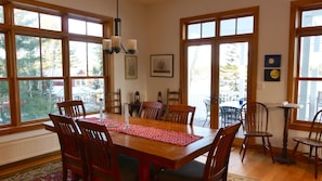 A dining area with a wooden table, chairs, and a red placemat. There are large windows with multiple panes, a chandelier, and framed pictures on the walls. -  New Well Built Elegant Home on the Water 2 miles to Freeport, 9  to Portland! (South Freeeport)