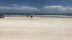 Uma praia com céu claro, algumas pessoas e um posto de salva-vidas.