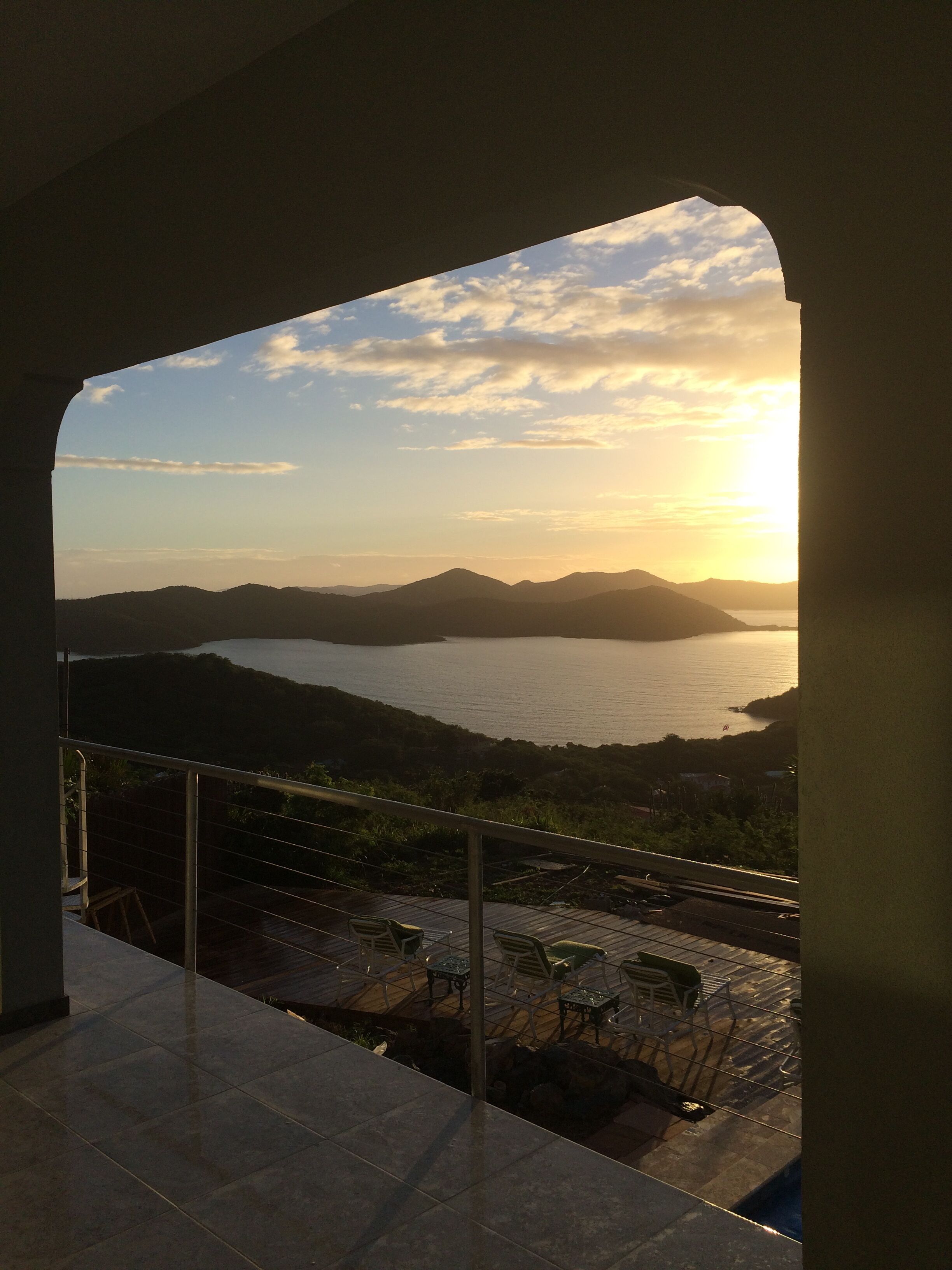 A balcony with a view of a sunset over a body of water and mountains.