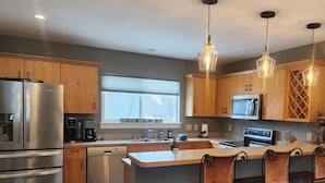 A modern kitchen with stainless steel appliances, wooden cabinets, and a bar area with stools. - Cozy Big Sky Chalet - Perfect For Your Montana Getaway (Big Sky)