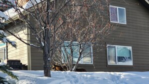 A house with a snow-covered yard and a tree in front. - Cozy Big Sky Chalet - Perfect For Your Montana Getaway (Big Sky)