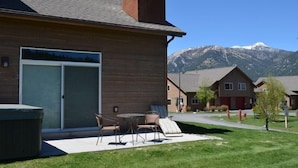 A modern building with a large garage door, outdoor seating area, and a mountain view. - Cozy Big Sky Chalet - Perfect For Your Montana Getaway (Big Sky)