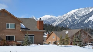 A modern two-story building with a wooden facade, a garage, and a view of snow-covered mountains. - Cozy Big Sky Chalet - Perfect For Your Montana Getaway (Big Sky)