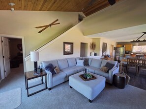 A spacious living room with a large sectional sofa, a coffee table, and a dining area with wooden chairs.
