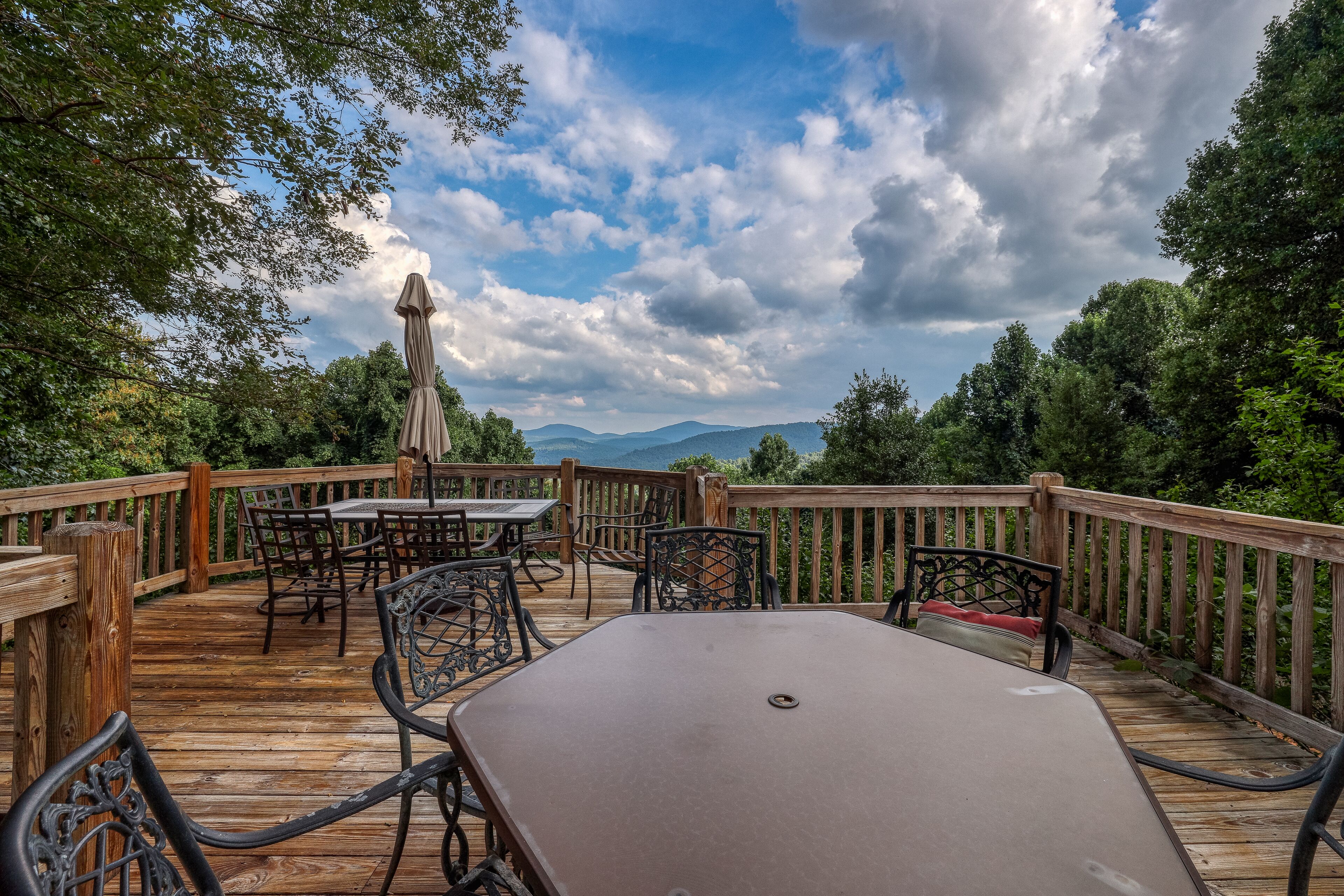 Una terraza de madera con mobiliario exterior, incluyendo una mesa y sillas, con vista a un paisaje montañoso.
