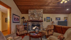 Una sala de estar acogedora con una chimenea de piedra, sillones a rayas y una mesa de centro con revistas.