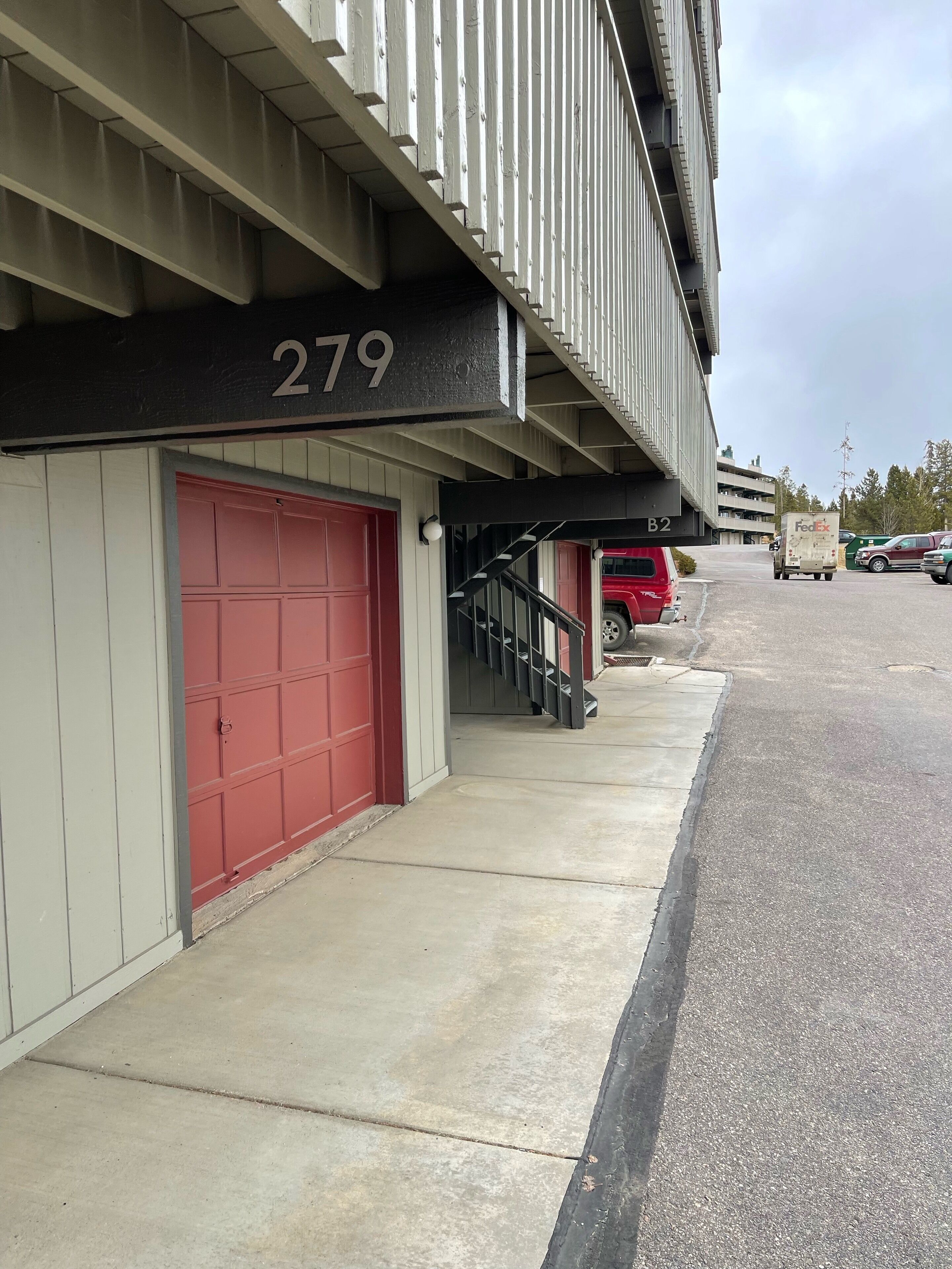 A building with a red garage door, a number '279' sign, and a FedEx truck parked on the street.
