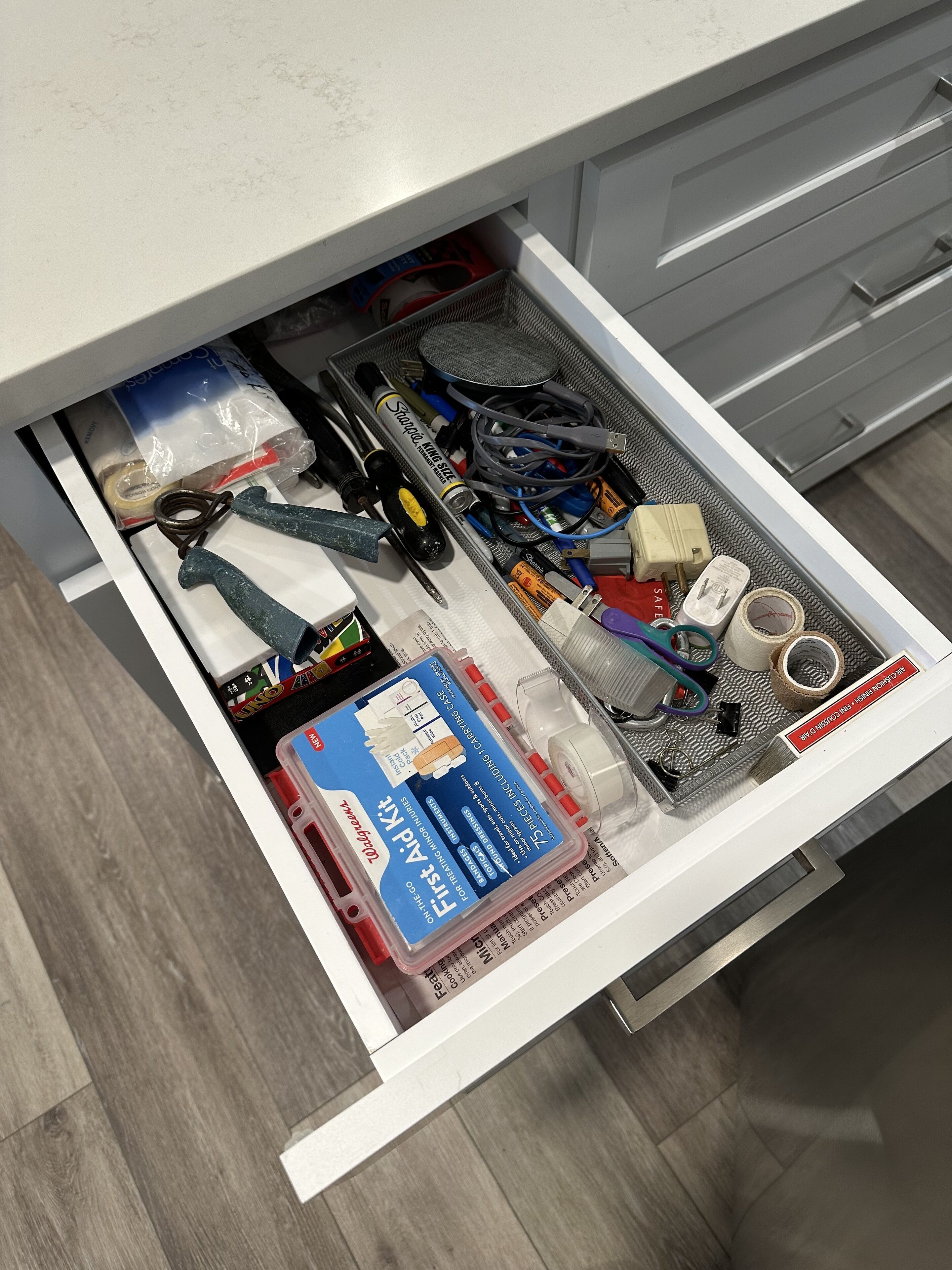 A drawer filled with various tools and supplies, including a box labeled "Fleece A.P.K." and several rolls of tape.