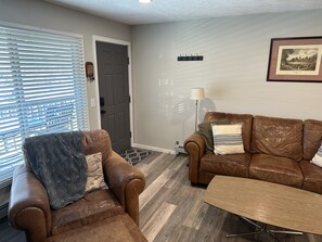 A living room with a brown leather sofa, a matching armchair, and a wooden coffee table.