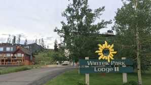 Schild für Winter Park Lodge II mit Sonnensymbol, umgeben von Grün und einer Straße.