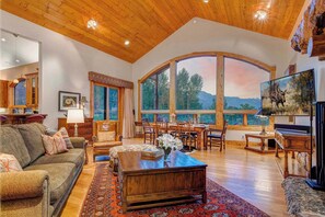 A spacious living room with a large window, wooden ceiling, and a cozy fireplace.