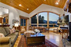 A spacious living room with a large arched window, wooden ceiling, and a cozy fireplace.