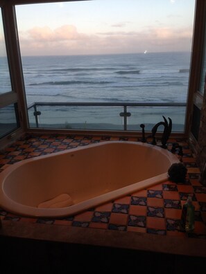 Ein Badezimmer mit einer großzügigen Badewanne, Meerblick durch ein Fenster und einem gefliesten Boden.