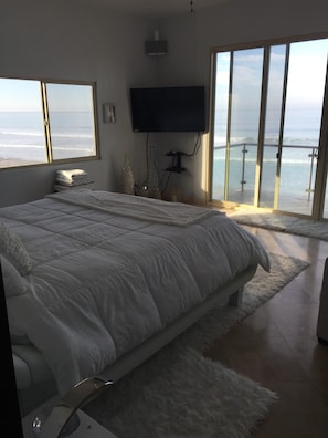 Ein Schlafzimmer mit einem großen Bett, einem an der Wand befestigten Fernseher und Meerblick durch die Fenster.