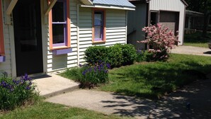 A single-story house with a front porch, a garage, and a small garden with purple flowers.