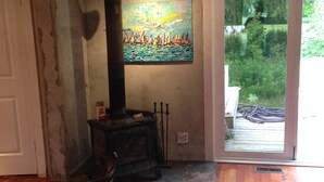 A cozy room with a wooden ceiling, a fireplace, a painting of sailboats, a dining table with chairs, and a rug.