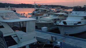 A marina with several boats docked, a clear sky, and a calm water body in the background.