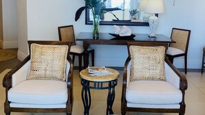 A living room with two wicker chairs, a coffee table, a side table, a mirror, and a vase with flowers. - "Sought-After" Luxurious 2100 sq ft Oceanfront Private Residence, in a Resort (Montego Bay)