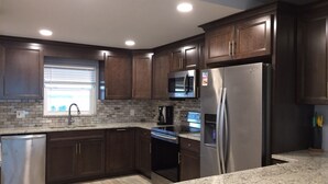 A modern kitchen with dark wood cabinets, stainless steel appliances, a granite countertop, and a window with blinds. - Paradise on the beach in an oceanfront, luxury condo on Sand Key (Clearwater Beach)