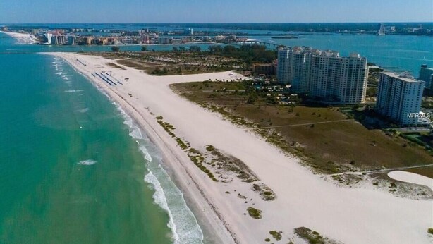 An aerial view of a coastal area with a long sandy beach, adjacent high-rise buildings, and a marina. - Paradise on the beach in an oceanfront, luxury condo on Sand Key (Clearwater Beach)