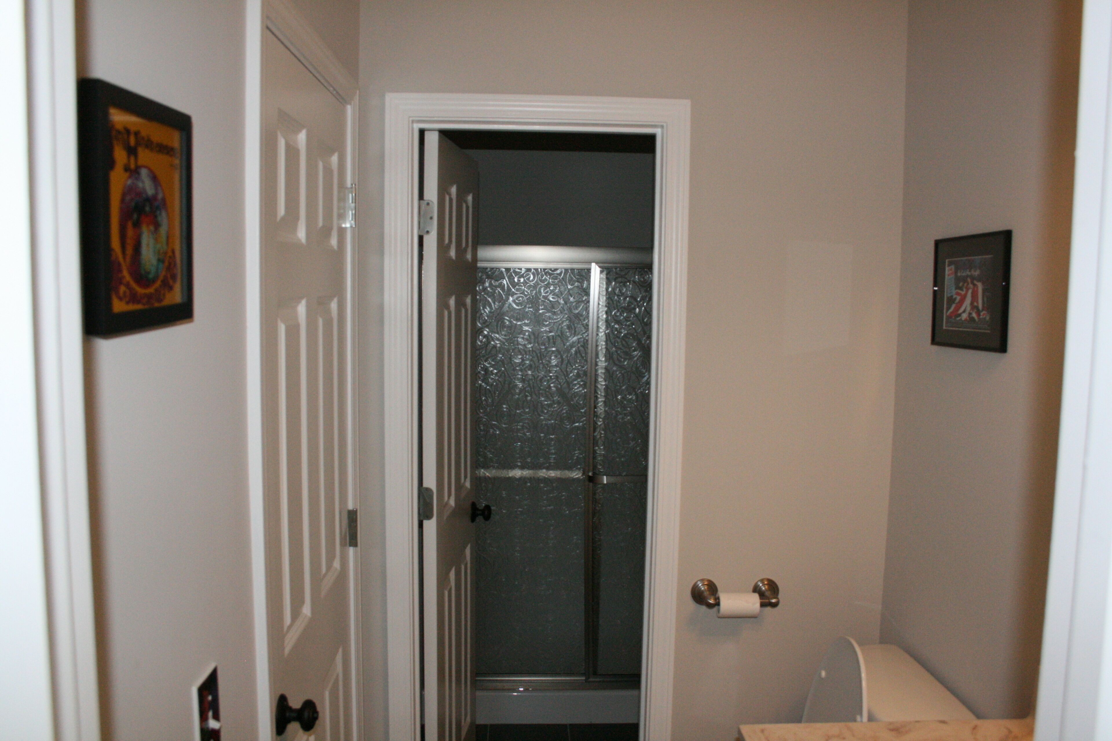 A narrow hallway with a door leading to a bathroom. The bathroom has a shower with a glass door and a toilet.