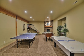 A room with ping pong tables, a foosball table, a fireplace, and a stone wall.