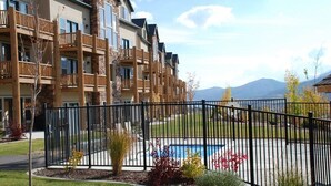 Un immeuble à plusieurs étages doté de balcons, d’une piscine et surplombant un paysage montagneux.