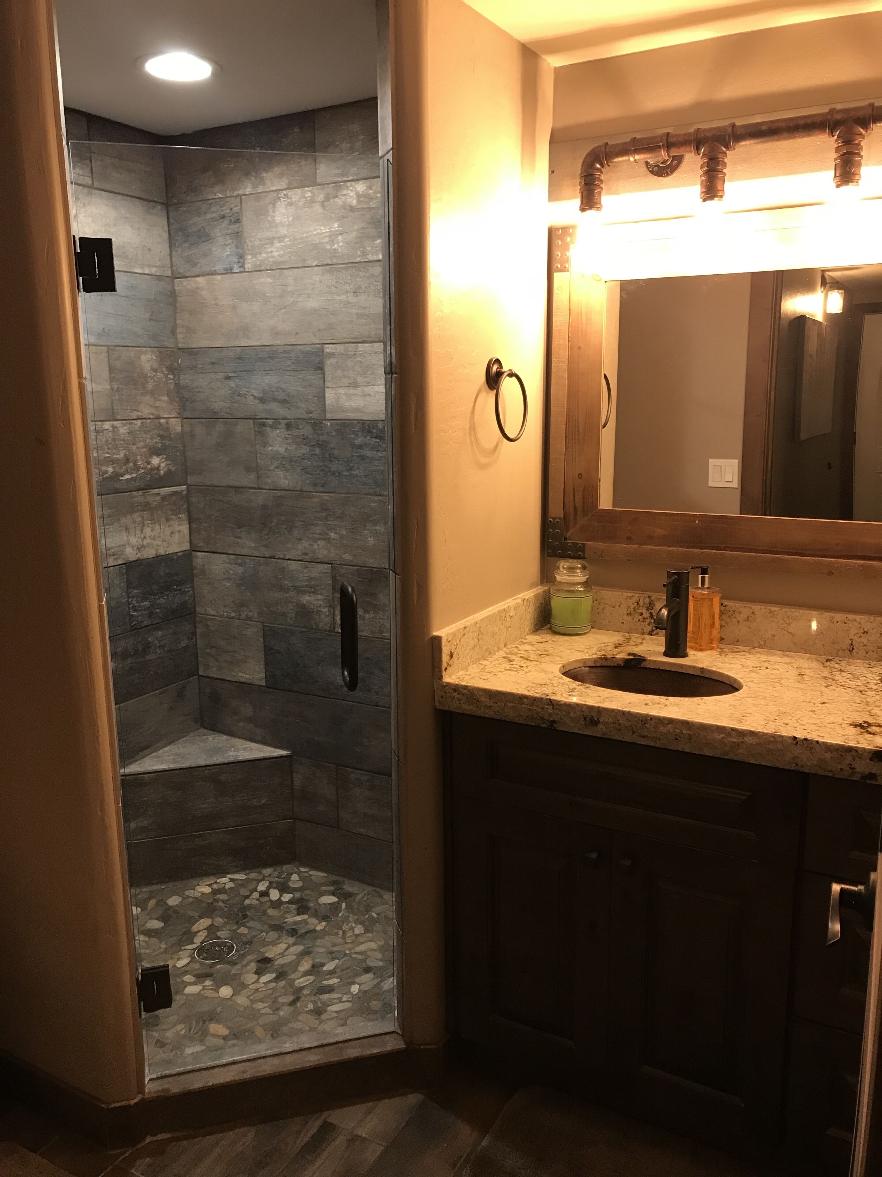 A bathroom with a stone shower enclosure, a vanity with a sink, and a large mirror.