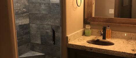 A bathroom with a stone shower enclosure, a vanity with a sink, and a large mirror.
