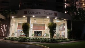 Entrada de un hotel con fachada de vidrio, dos plantas en macetas y un letrero que dice "Kaanapali Shores".