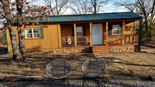A wooden cabin with a green roof, a porch with a railing, and two metal chairs in front. - Cabin for two on 160 Acres,less than 20 min from Choctaw Casino Durant OK (Bokchito)