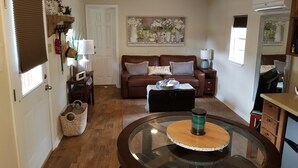 A cozy living room with a brown leather sofa, a glass coffee table, and a painting on the wall. - Cabin for two on 160 Acres,less than 20 min from Choctaw Casino Durant OK (Bokchito)
