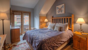 A bedroom with a bed, two bedside tables with lamps, a wooden headboard, a door, and a window. - Walk to Lifts! Free Covered Parking, High Ceilings (Dillon)